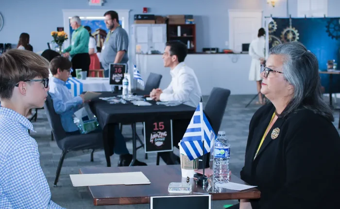Students from five Plato Academy campuses participate in the Amazing Shake final competition at Tampa campus on April 24, 2026, rotating through 25 challenge stations themed around a trip to Greece, practicing real-world communication and problem-solving skills with professional judges evaluating their composure, public speaking, and adaptability.